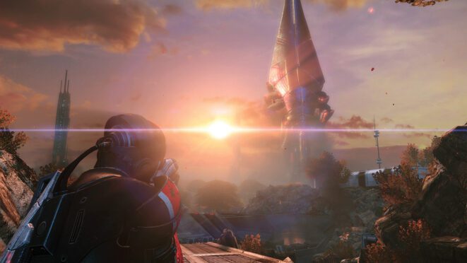 Commander Shepard, seen from behind in armor, looks toward a tall spire as the sun sets in Mass Effect Legendary Edition